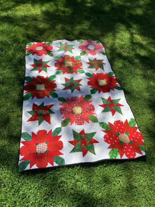 A red green and white rectangular Christmas quilt laid on grass's
