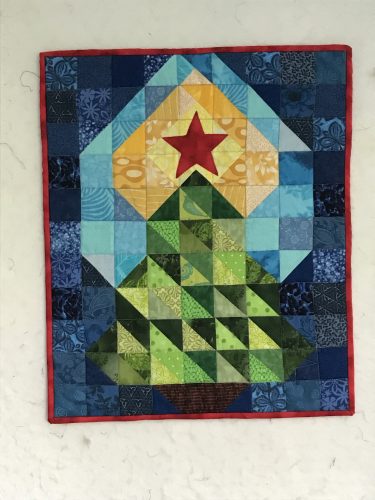 A rectangular Christmas tree quilt in blue, yellow, green, with a red star
