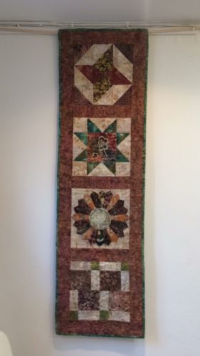 A rectangular 4 patch table runner in brown and green batik fabrics